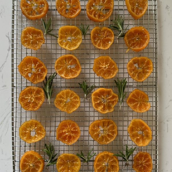 candied mandarins, decorated with rosemary sprigs, set on top of a cooling rack.