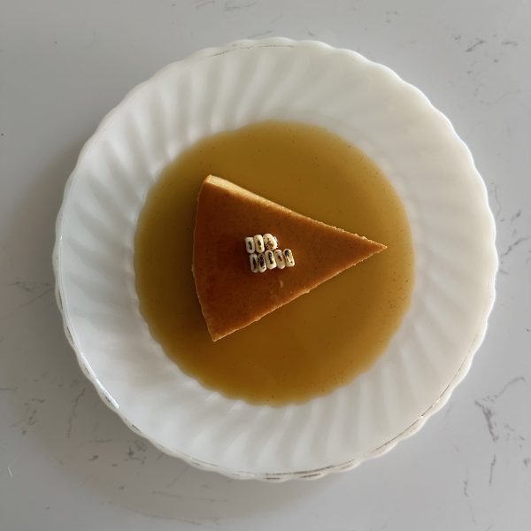 a slice of corn flan surrounded with caramel and topped with pieces of roasted corn kernels.