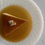a slice of corn flan surrounded with caramel and topped with pieces of roasted corn kernels.