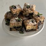 large, square pieces of blueberry mint coffee cake placed on top of a cake stand. the pieces are decorated with fresh blueberries and mint.