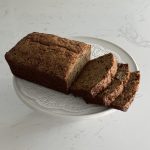 loaf and slices of rye banana bread on top of a white cake stand
