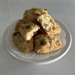 six white cheddar and black pepper biscuits, with one cut open, served on top of a white cake stand