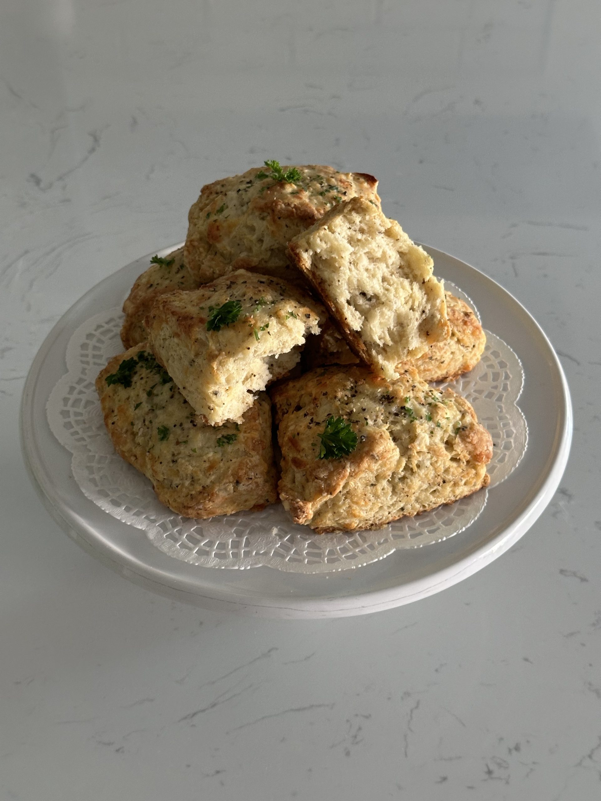 six white cheddar and black pepper biscuits, with one cut open, served on top of a white cake stand